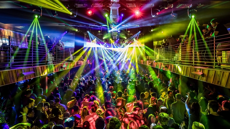 Wide BOH shot of the full production lights colored yellow, red, blue, and white illuminate the crowd on both the first floor and 2nd floor balconies.