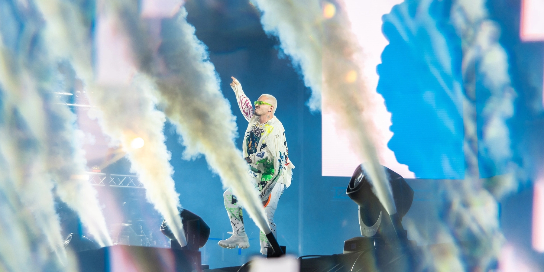 Bad Bunny center stage below the large "X BAJA BEACH FEST X" sign above the main stage. The production lights are blue and the visuals resemble abstract posters.