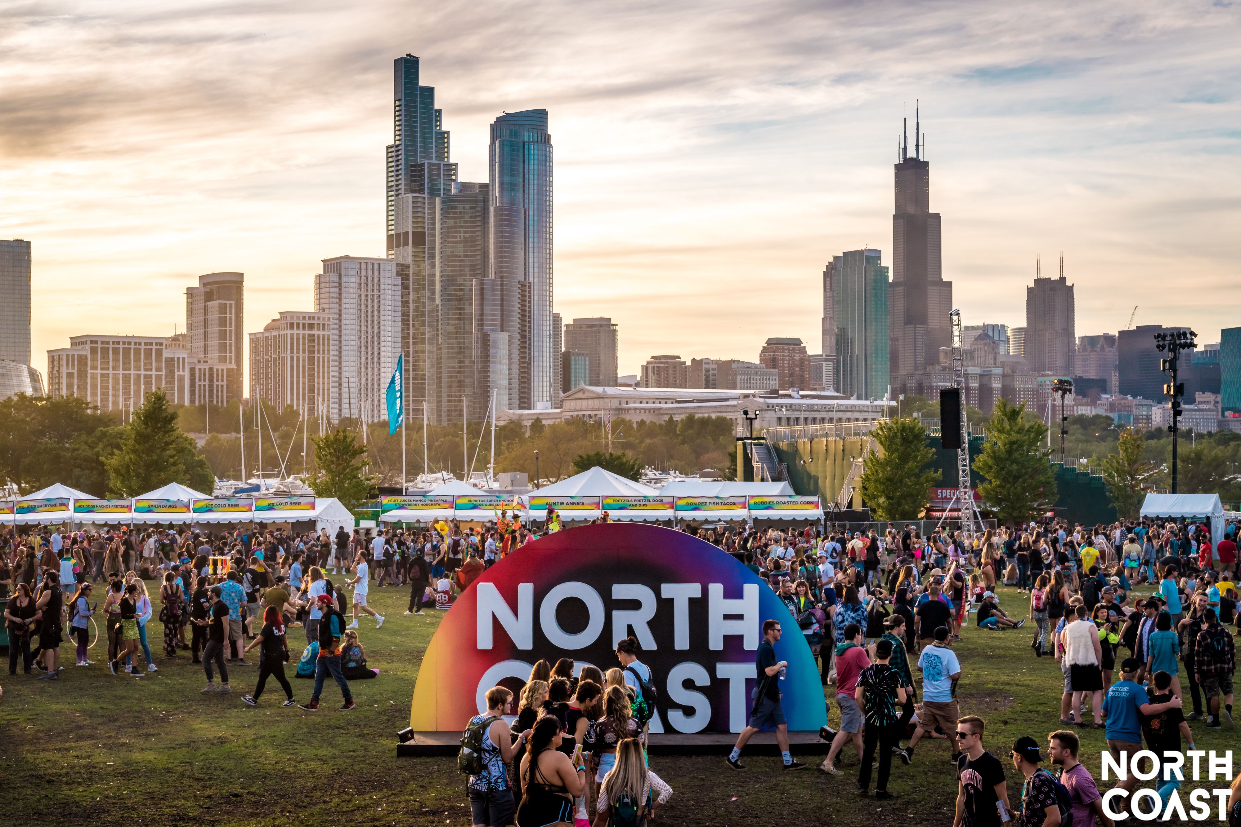 Drone shot of Huntington Bank Pavilion at Northerly Island as North Coast is occuring. There is a large North Coast sign in the center for experiential photos and a large number of people congregating around the festival grounds.