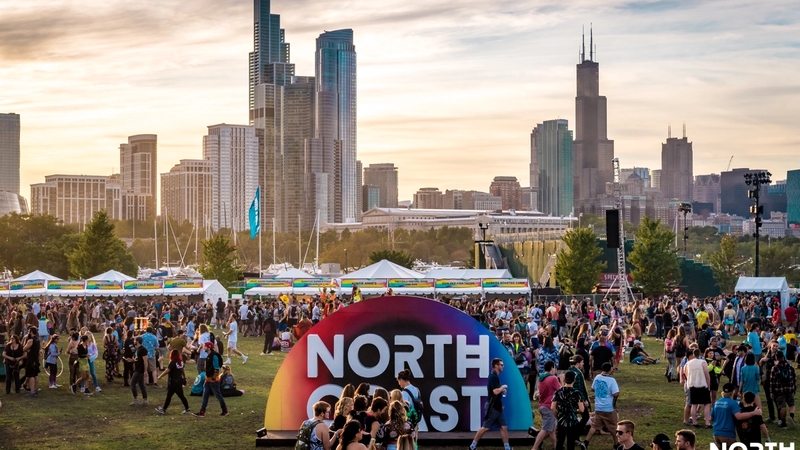 Drone shot of Huntington Bank Pavilion at Northerly Island as North Coast is occuring. There is a large North Coast sign in the center for experiential photos and a large number of people congregating around the festival grounds.