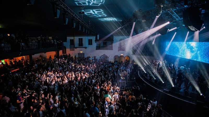 Side stage view of Ramova Theatre stage from the Artist balcony with white lights shining and a top-view of the crowd