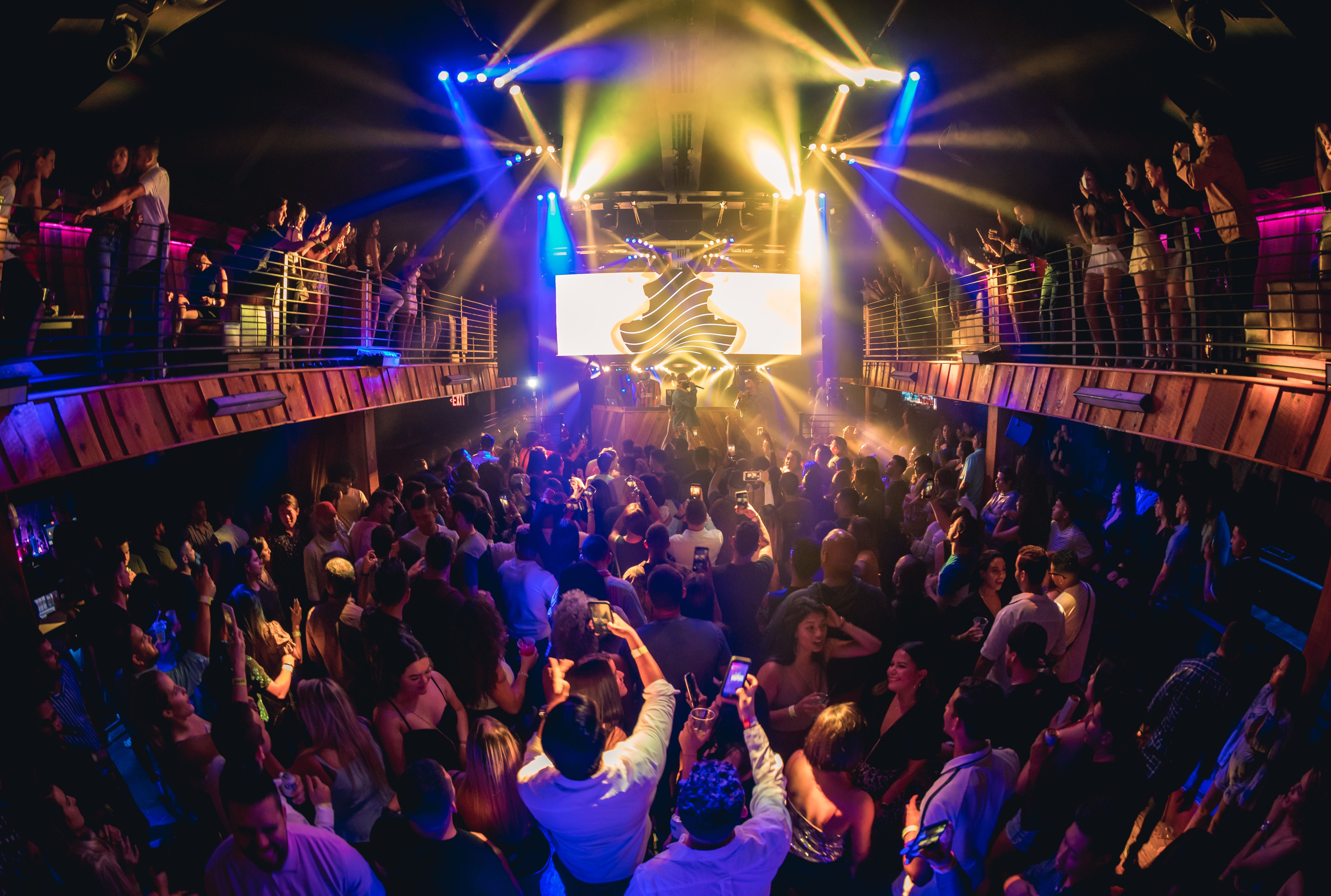 Wide BOH shot of a full crowd at Ravine as an artist performs. The crowd is also on either side on the balconies as the production lights shine yellow and blue on the crowd