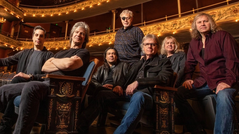 The band Kansas sitting in a theater. All but one member are sitting.