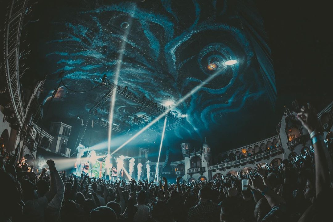 Wide shot of the Byline Bank Aragon Ballroom ceiling with abstract galaxy like painting. CO2 shoots off over a large packed crowd on the dance floor. 