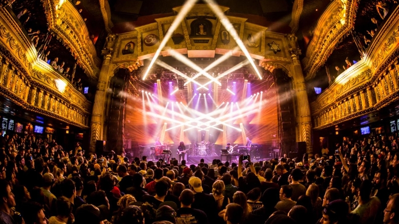 Wide front of house shot of the House of Blues stage with a large crowd standing in front. There are people on either side going up 2 more floors on the balconies.
