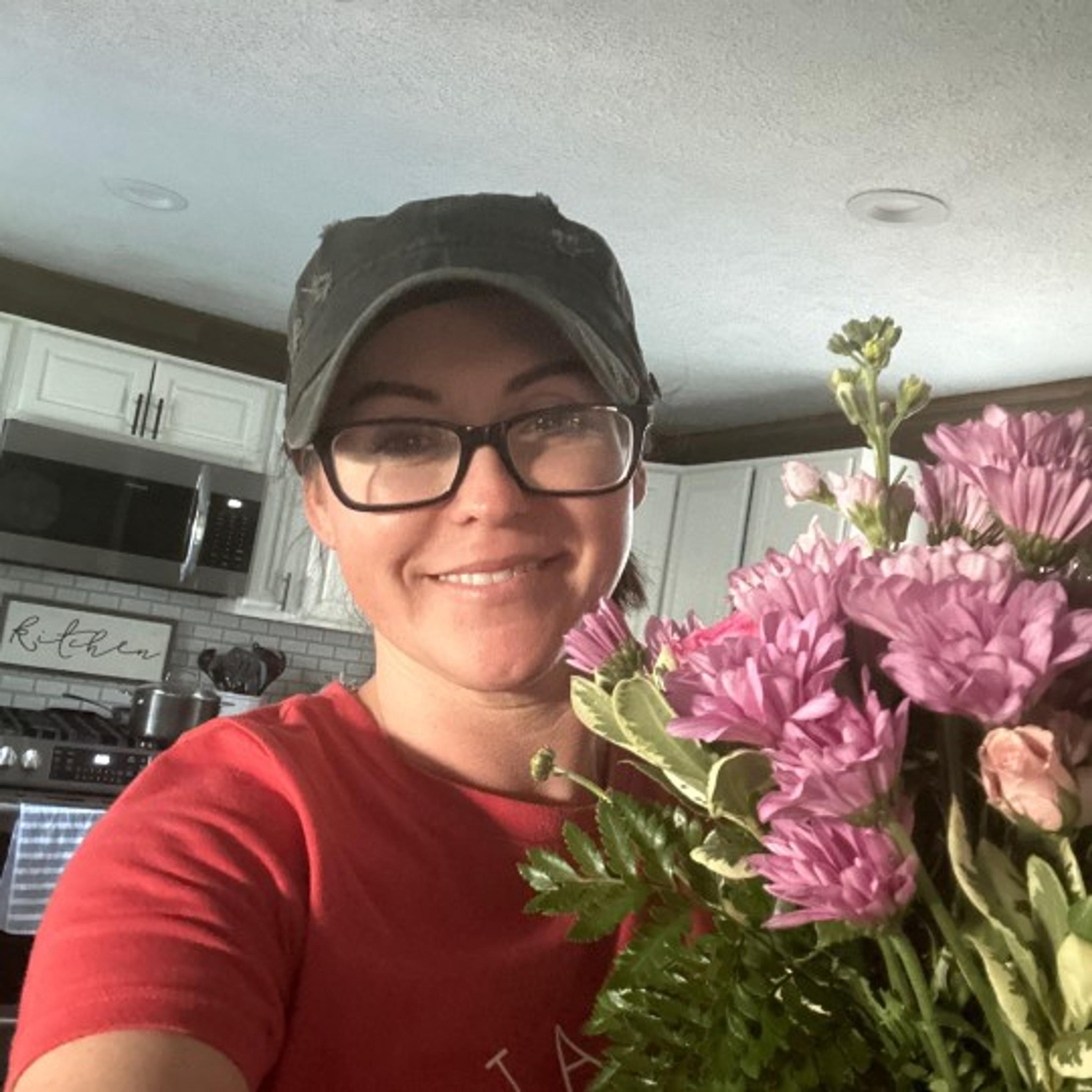 Woman wearing black hat and black sunglasses holding pink flowers and smiling, thankful for flowers