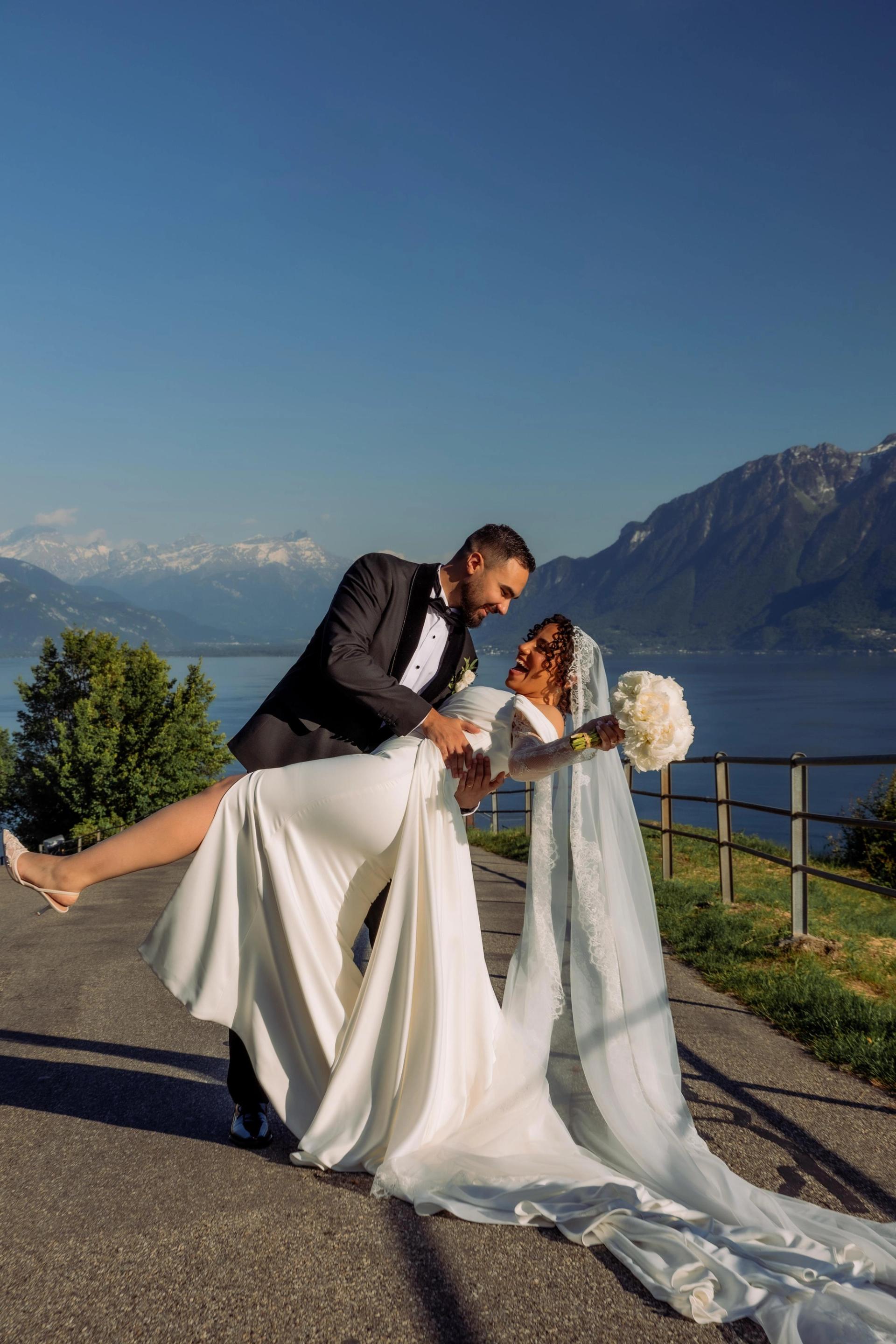 Rafaël porte Julia dans sa robe de mariée face au lac et aux montagnes suisses