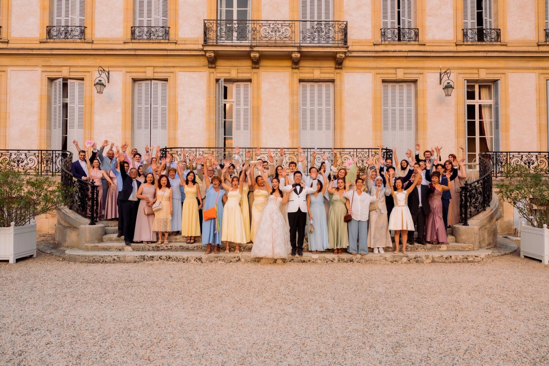 Photo de groupe des mariés et de leurs invités devant le château