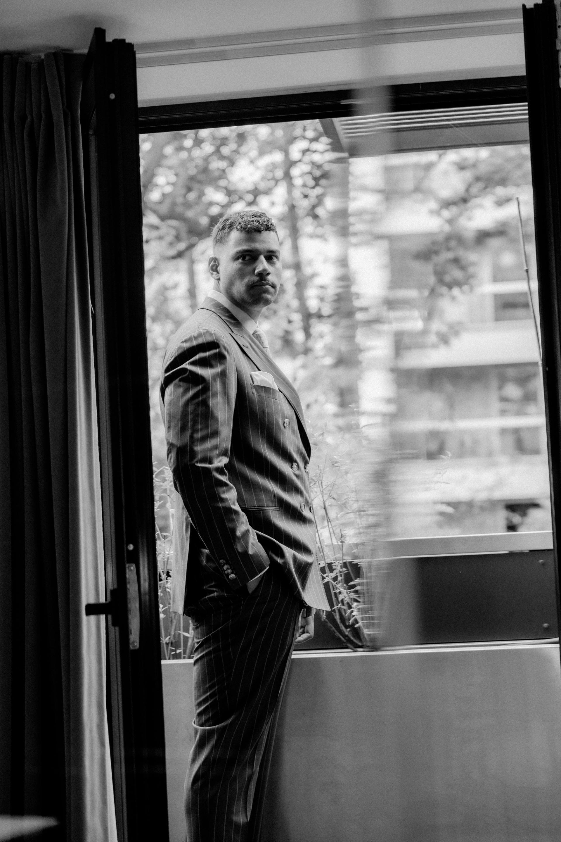William ajuste sa tenue près d’une fenêtre en noir et blanc