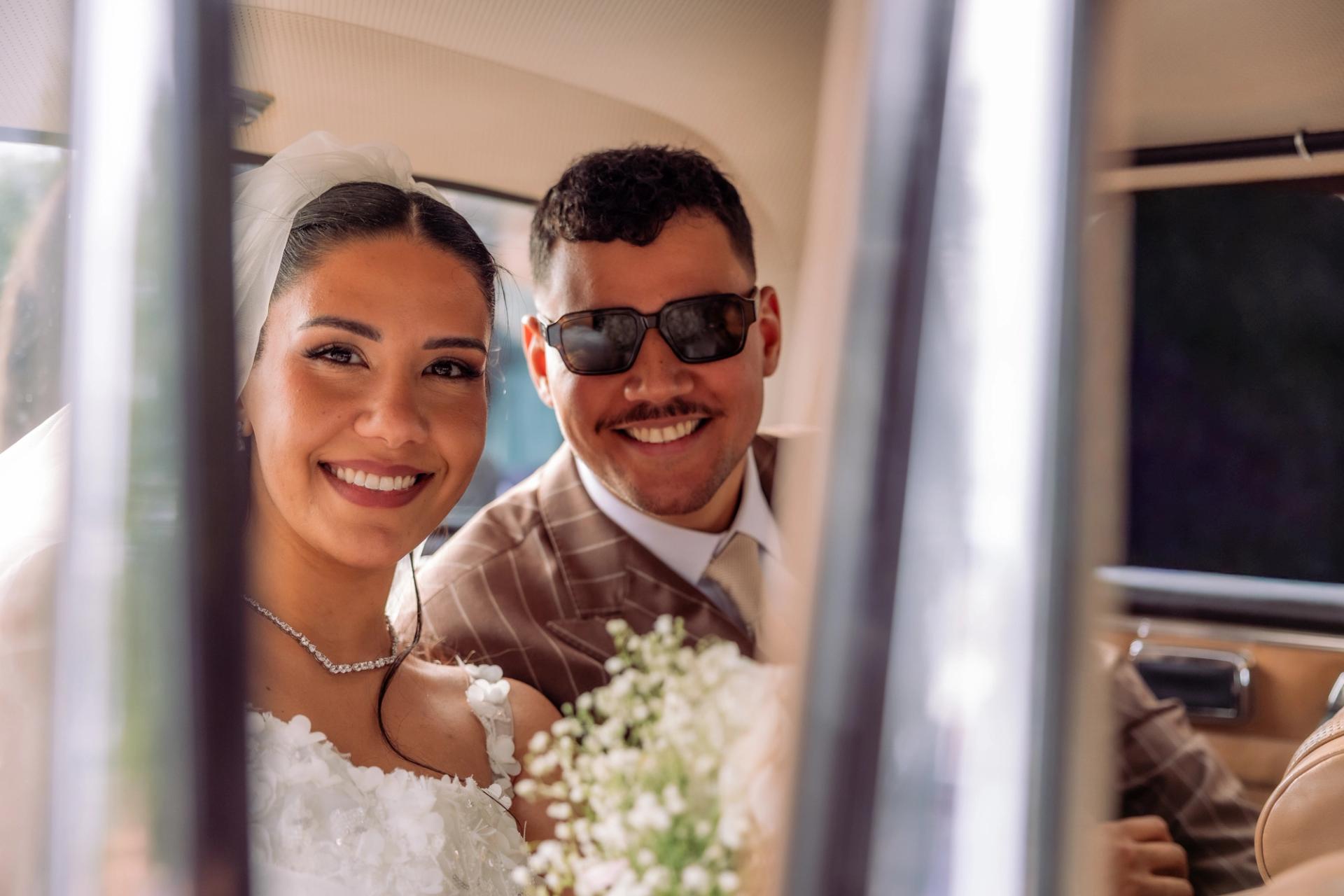 Les mariés posent dans la voiture avec des lunettes de soleil
