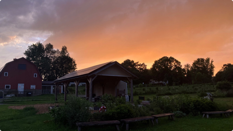 An orange sky is illuminated orange as the sunsets over the Massaro Farm Solar Pavilion.