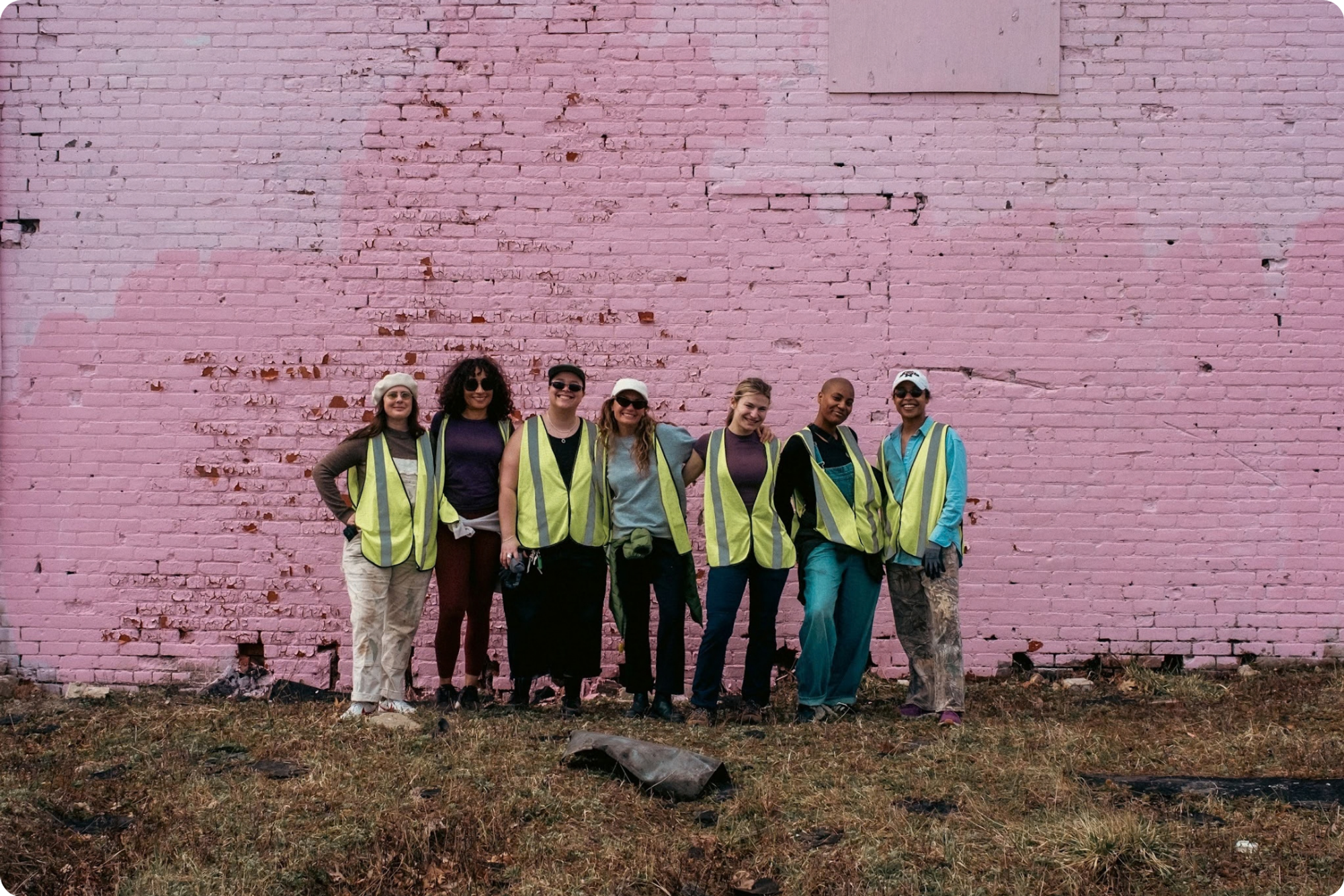 A group of people in hi-vis vests pose in front of a pink wall
