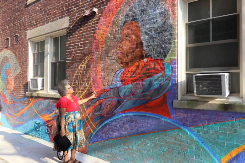 A Black woman touches and views a new mural depicting herself with swirling colors.