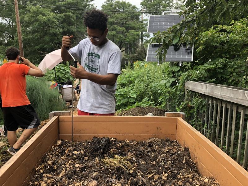 A young Black man amends the soil in a raised garden bed. 