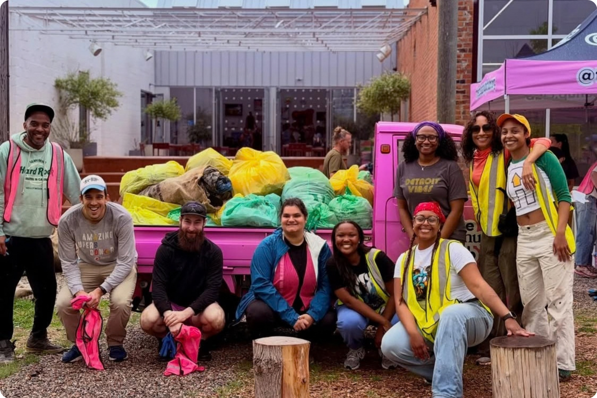 A team of volunteers in hi-vis vests pose together in front of a bright pink dumpster, filled with full rubbish bags.