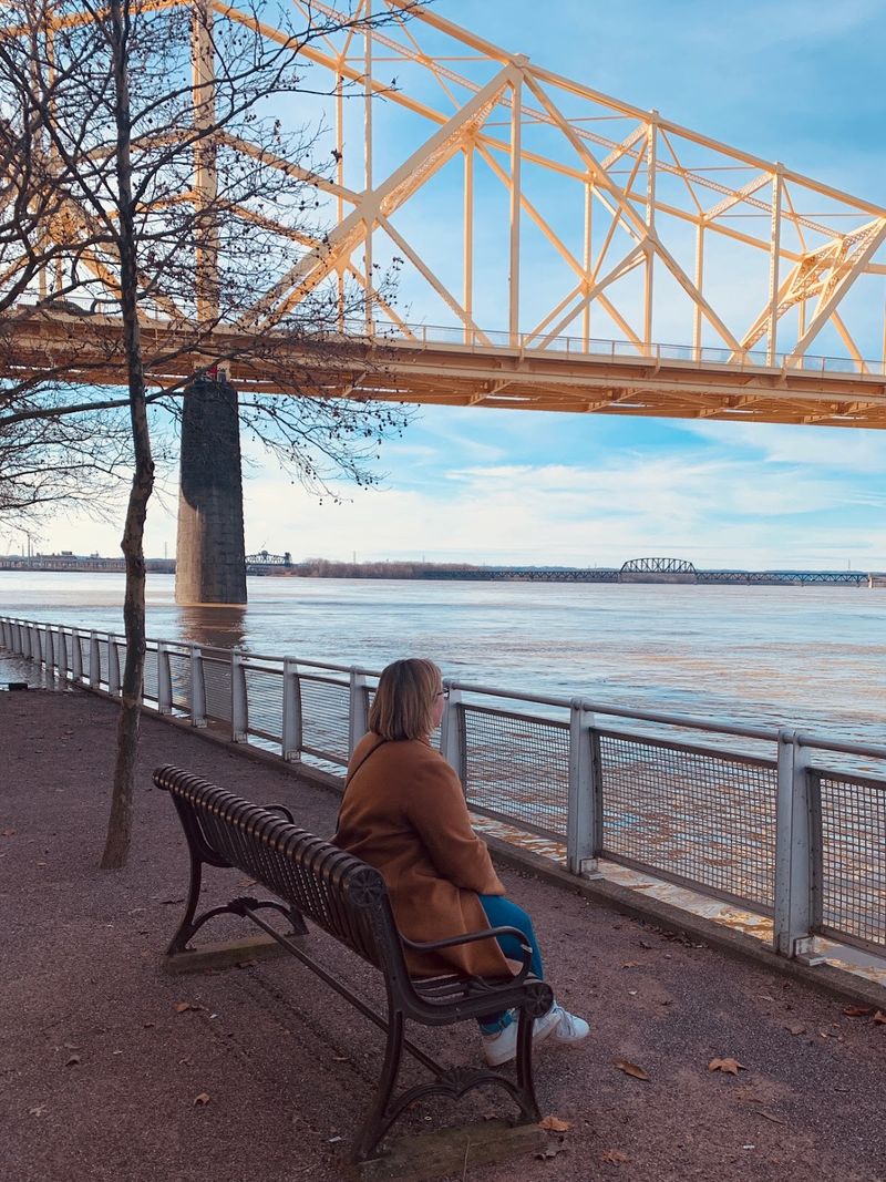 Bridget sits on a Bench facing the Ohio River under a bridge overpass