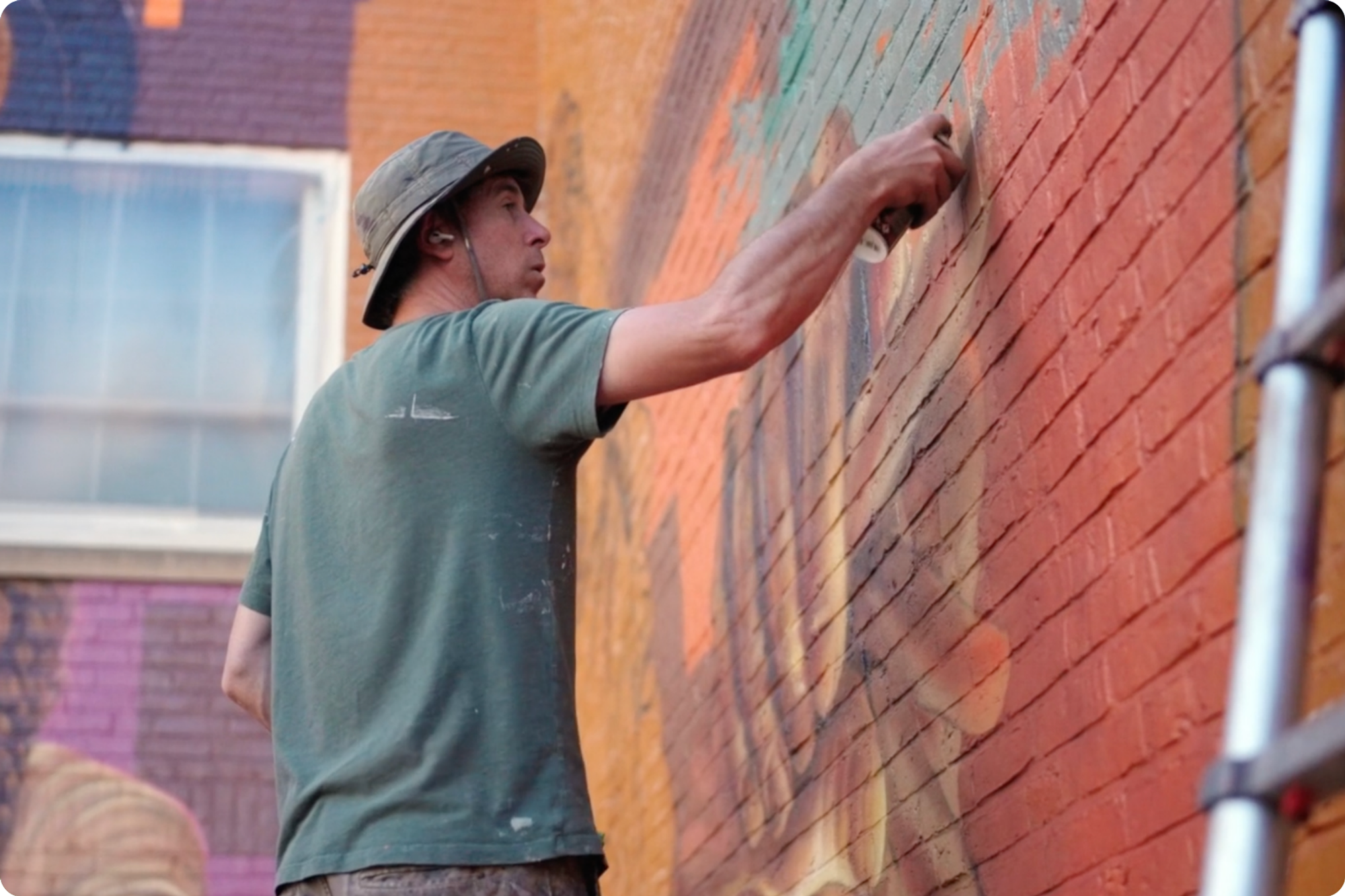 A man, Michael Rice, paints the mural with a spraycan. 