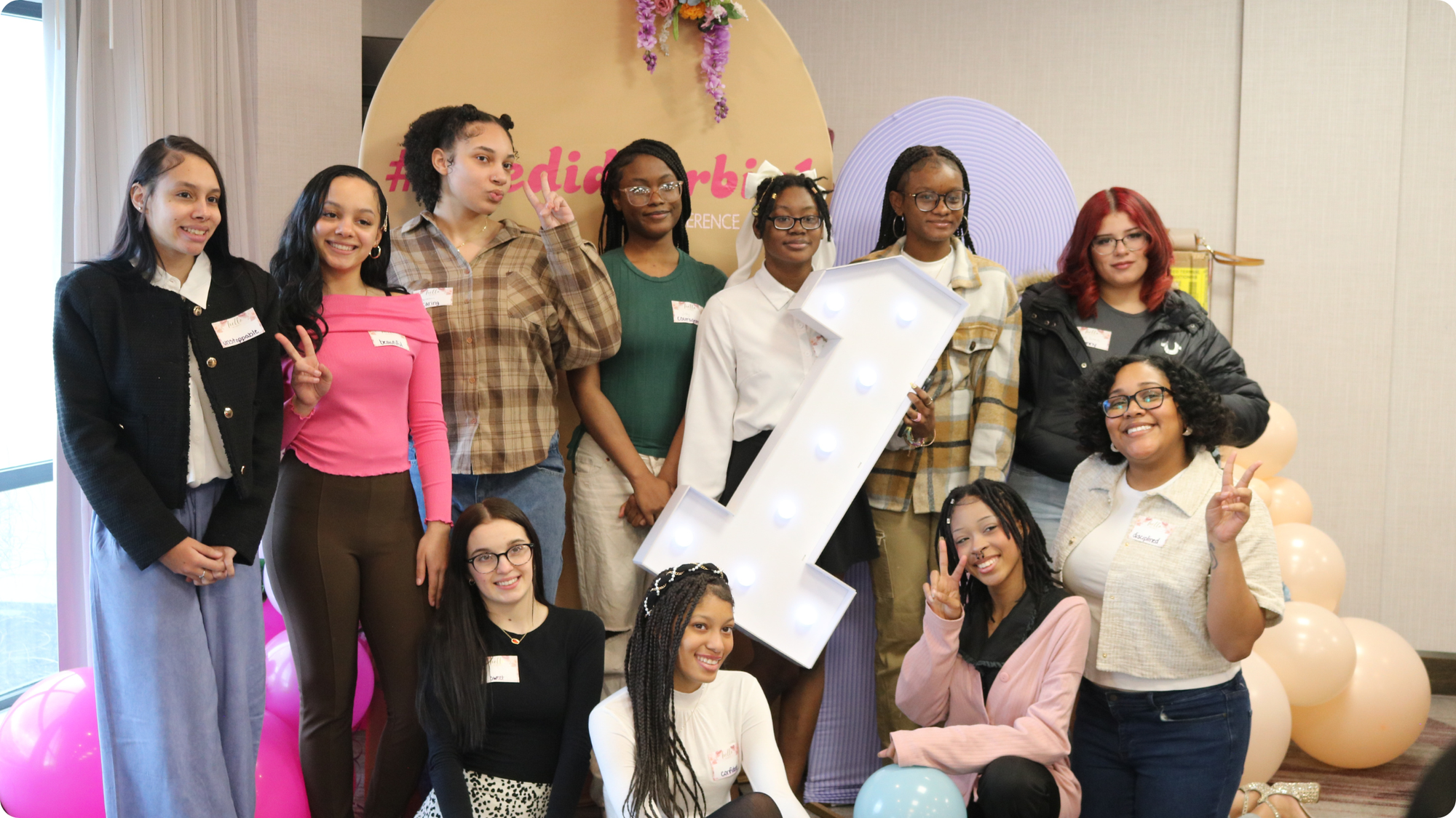 A group of high school girls throw up peace signs at the "She Did Her Big 1" Conference.