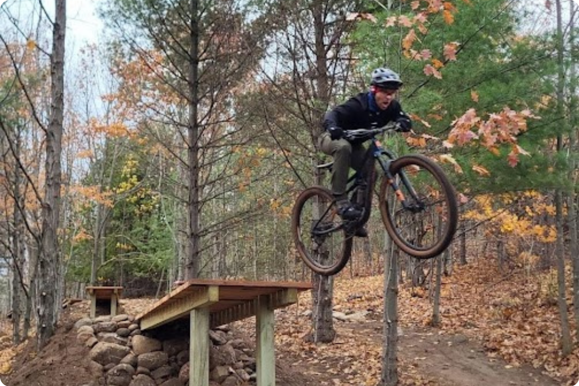 A man on a mountain bike soars off a new trail ramp in the woods.