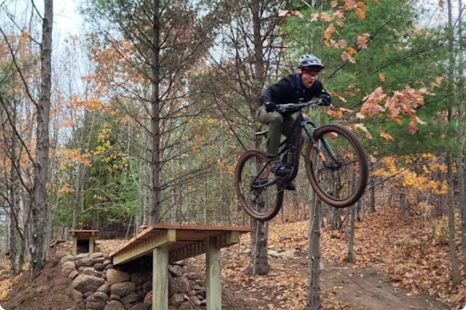 A man on a mountain bike soars off a new trail ramp in the woods.