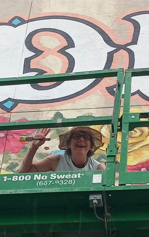 One of the mural artists waves with a paint brush in hand from the lift during installation.