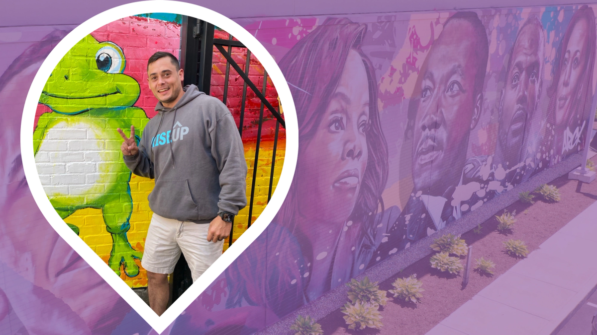 Matt Conway, a white middle-aged man, poses with a peace sign in front of a frog mural.