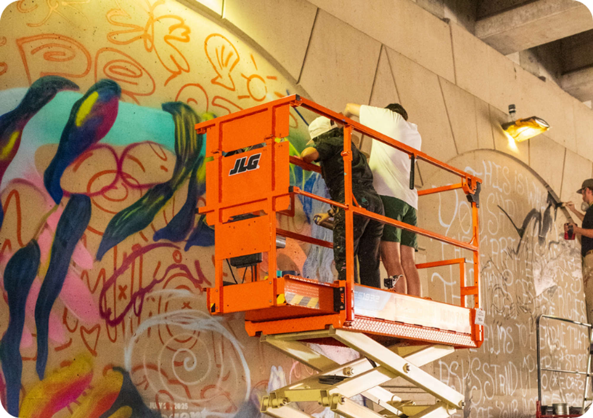 Artists atop an aerial lift work on their underpass mural