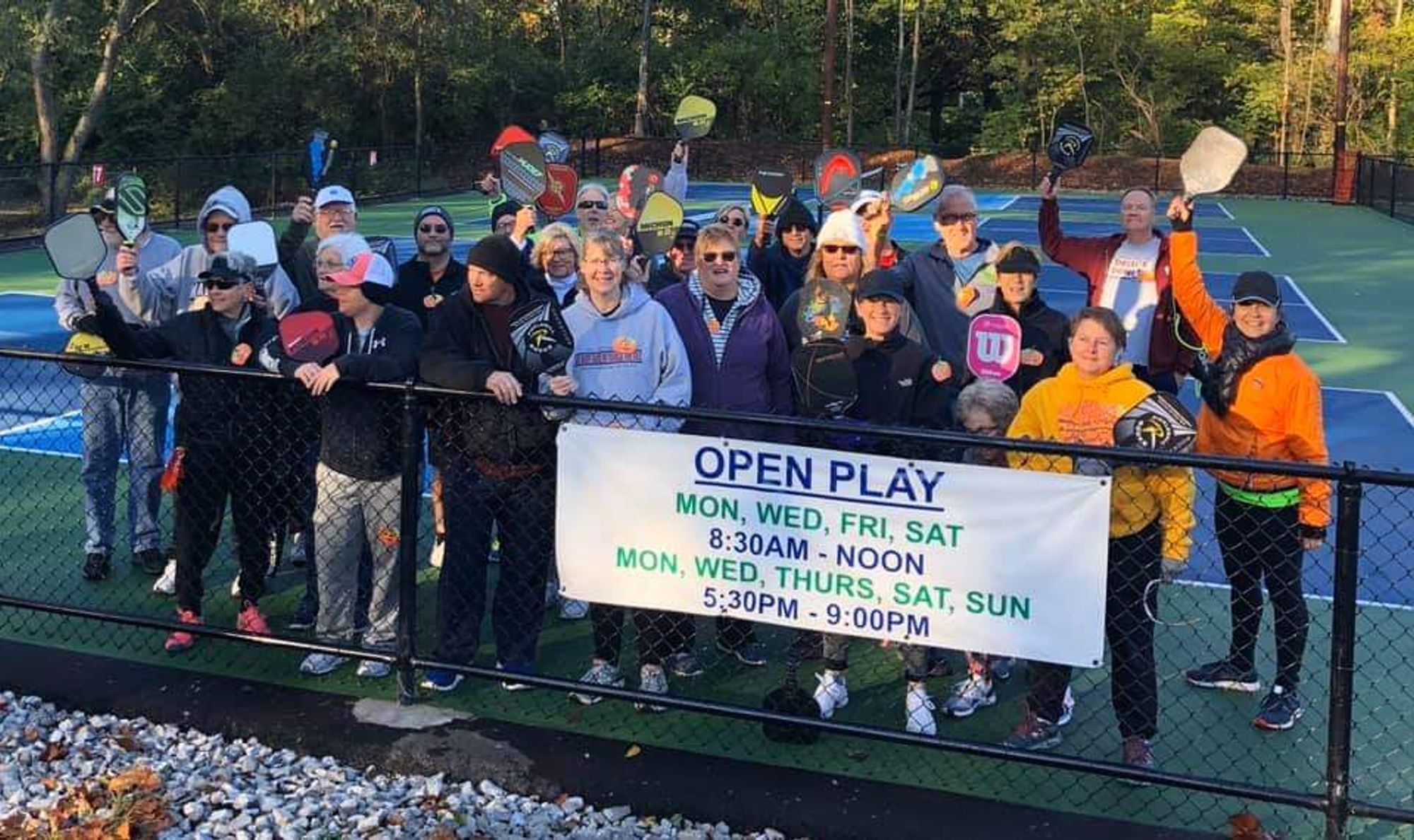 A group of Pickleballers hold their paddles to the sky and smile to the camera on their new course. 