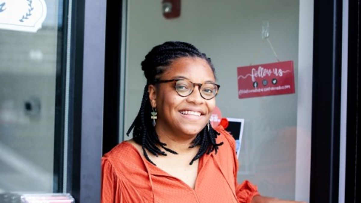 Jae'da Turner stands with the door open to her small business with a smile on her face.