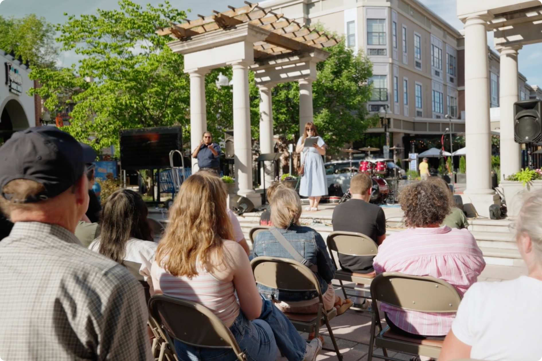 The crowd watches the opening remarks of the unveiling ceremony, with Megan and an ASL interpreter on the stage.