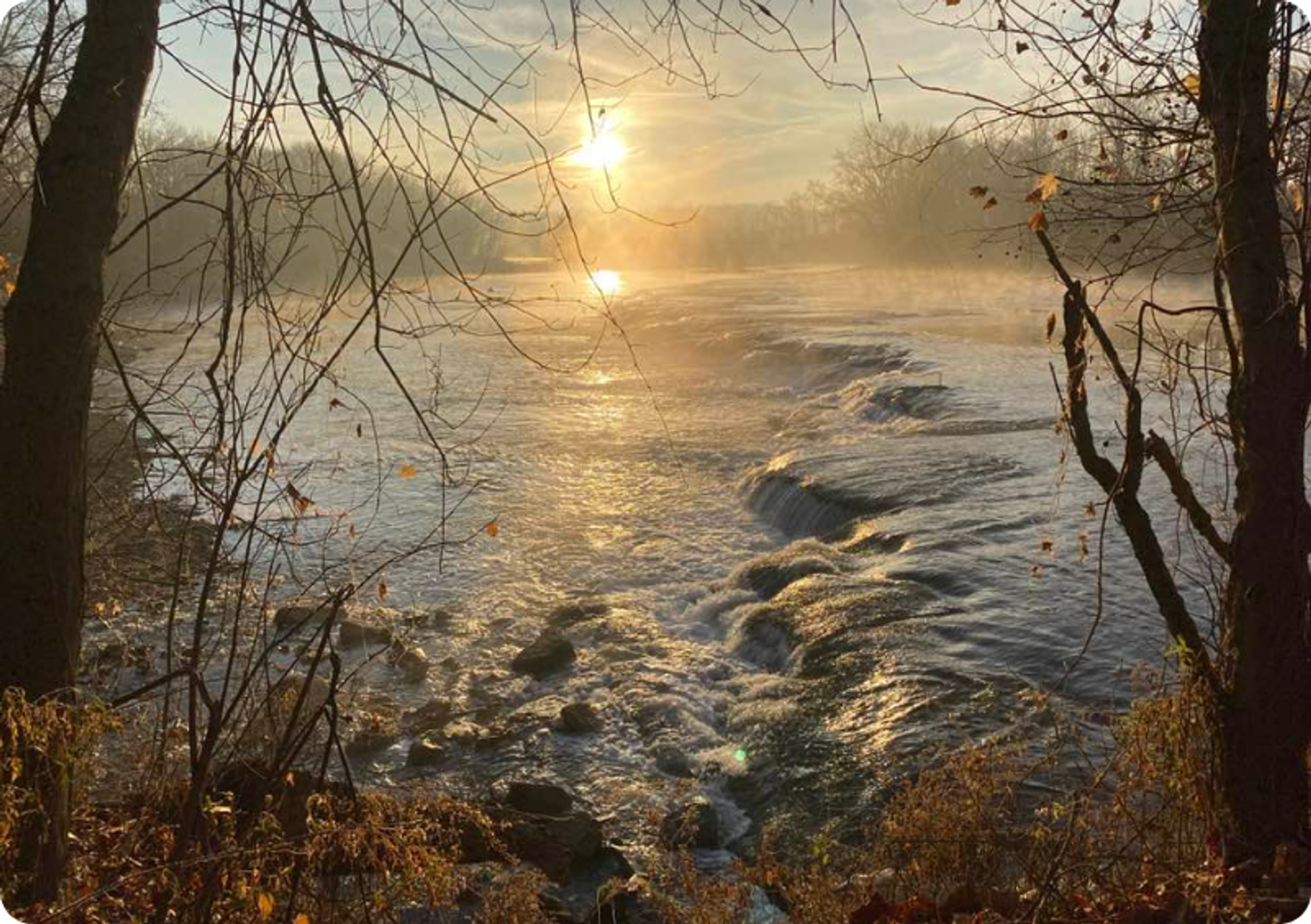 Sunset over a rushing river with trees framing the foreground