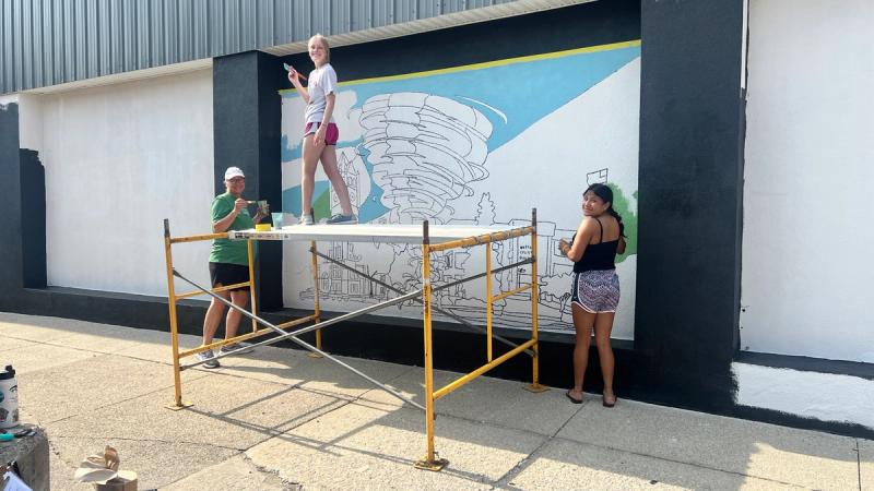Three students work to paint a mural project in Monticello, Indiana