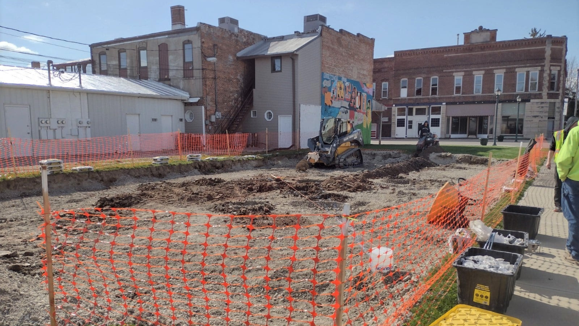 Construction of Arcadia Splash Pad in Arcadia, Indiana. An empty dirt lot is surrounded by orange construction fencing.
