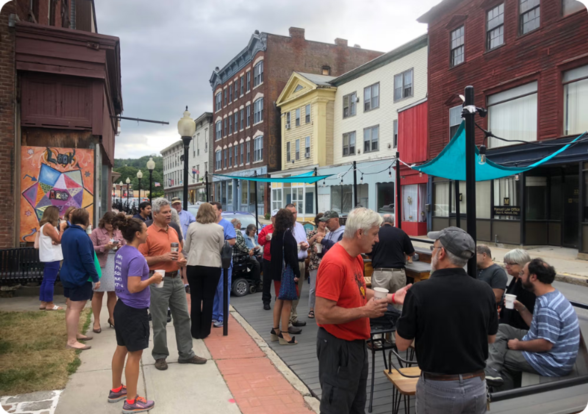 People mill about on a pedestrian street fitted with benches, tables, and shade cloths.
