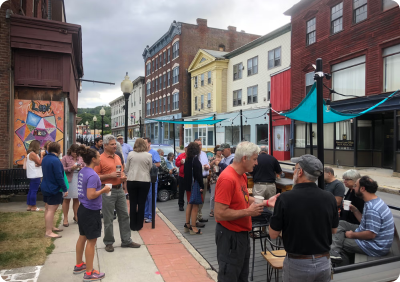 People mill about on a pedestrian street fitted with benches, tables, and shade cloths.