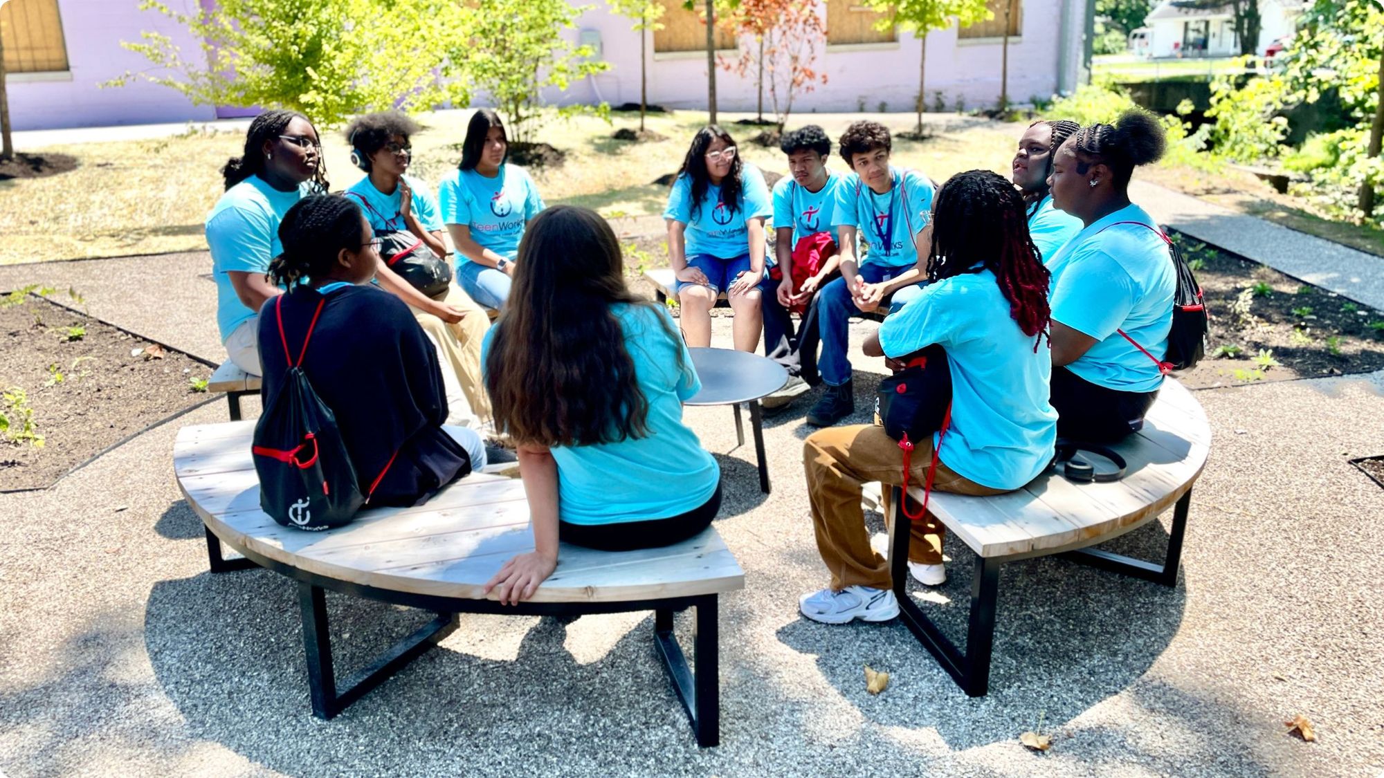 A group of teenagers sit at a circular bench area in a garden.