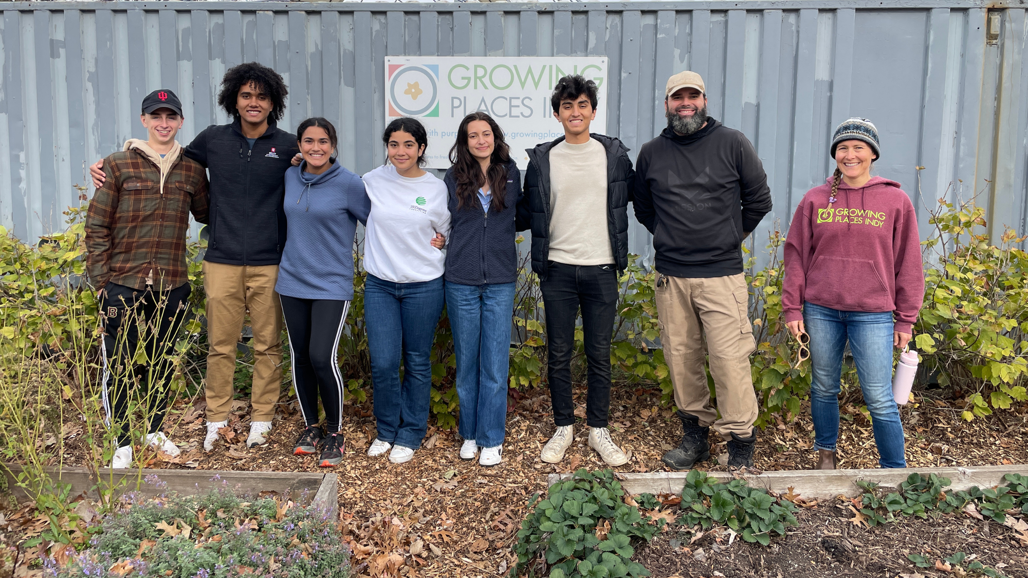 Growing Places Indy volunteers stand arm-in-arm and smile at the camera in a community garden.