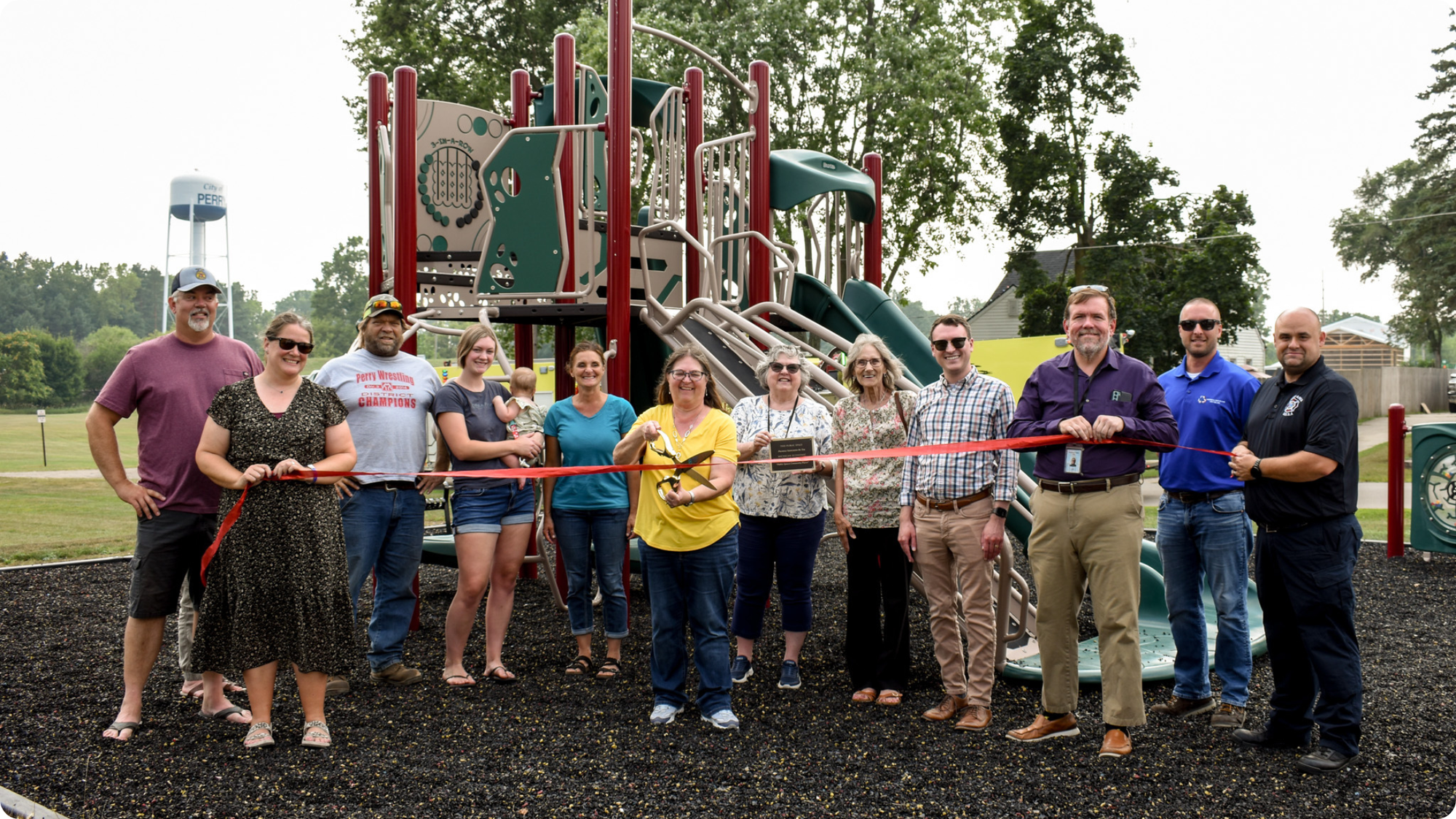 A group of residents cut a red ribbon to open the City of Perry Veteran's Memorial Park Playground.
