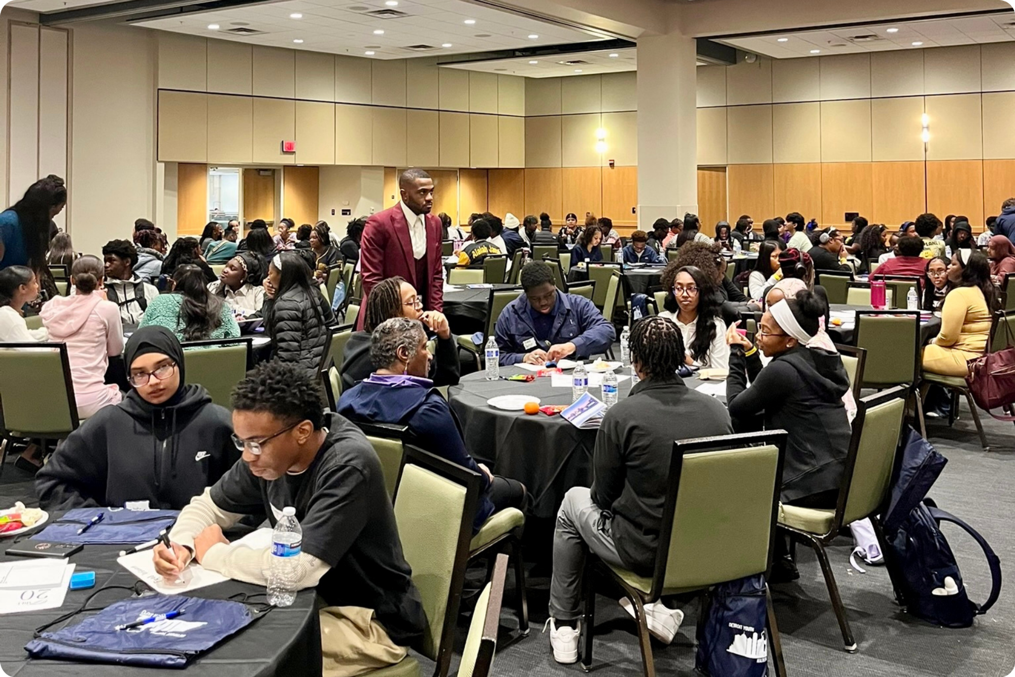 A conference room full of students sitting and chatting at round tables.