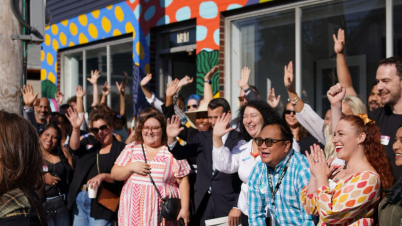 The opening of EmVision Productions studio space. The community cheers, excited in front of EmVision’s new space, which features a colorful mural. 