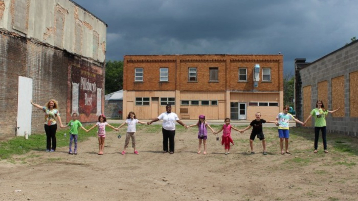 A group of kids hold hands in a long line for a crowdfunding campaign image.