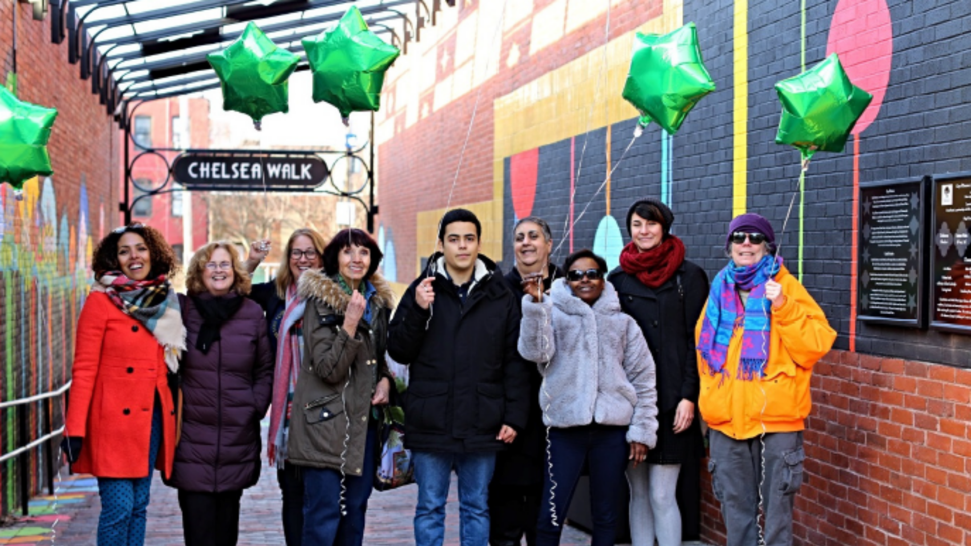 A group of community members celebrate the opening of their renewed public space with green balloons in their hands.