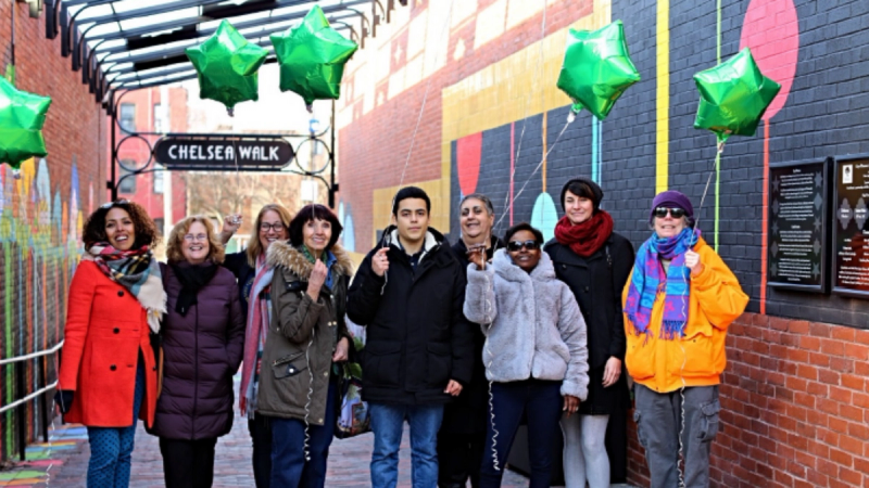 A group of community members celebrate the opening of their renewed public space with green balloons in their hands.