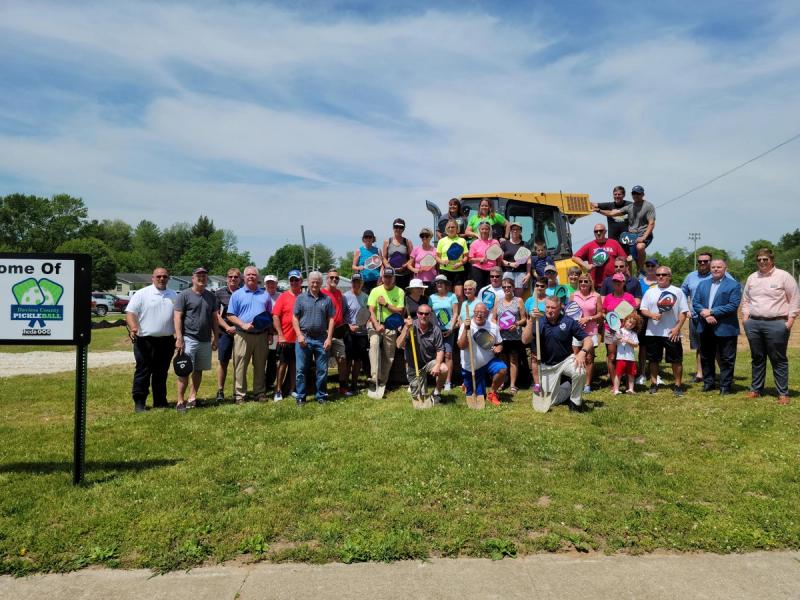 The groundbreaking of the Daviess County Pickleball Court. People gather around a large digger in celebration.