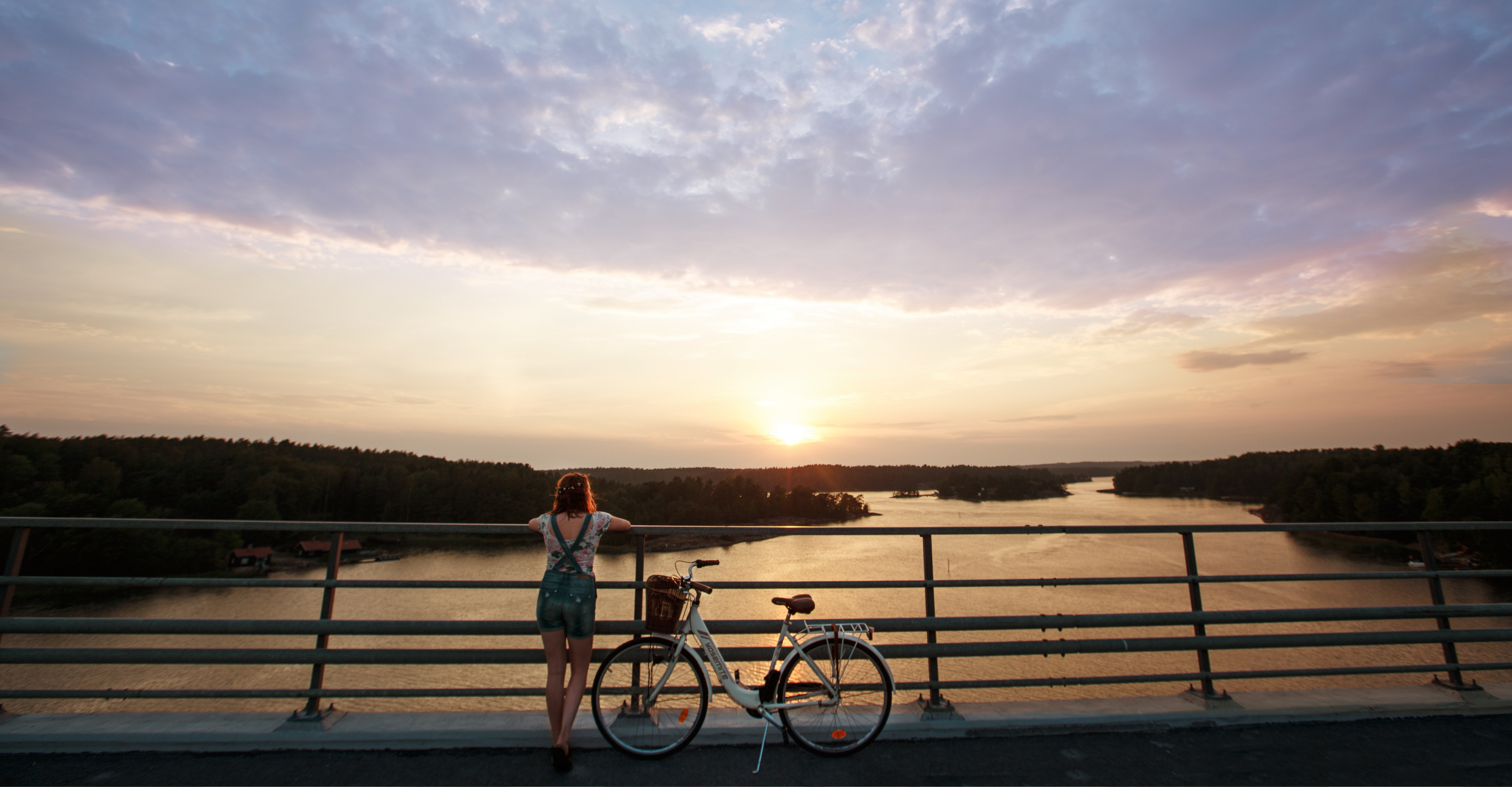 A person with her bicycle on a bridge admiring the sunset over the Finnish archipelago.