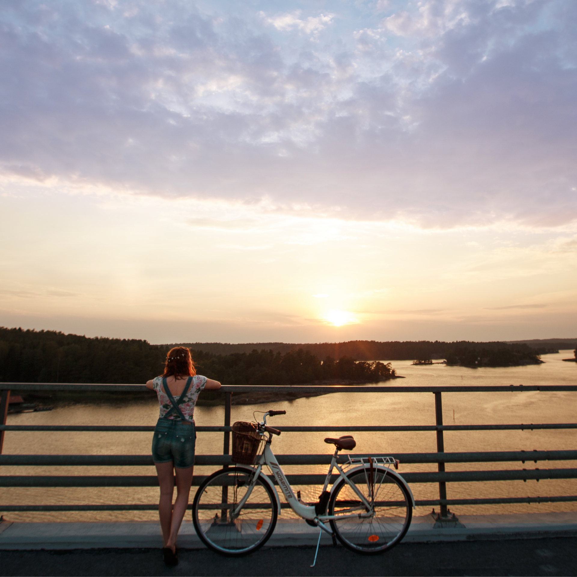 A person with her bicycle on a bridge admiring the sunset over the Finnish archipelago.