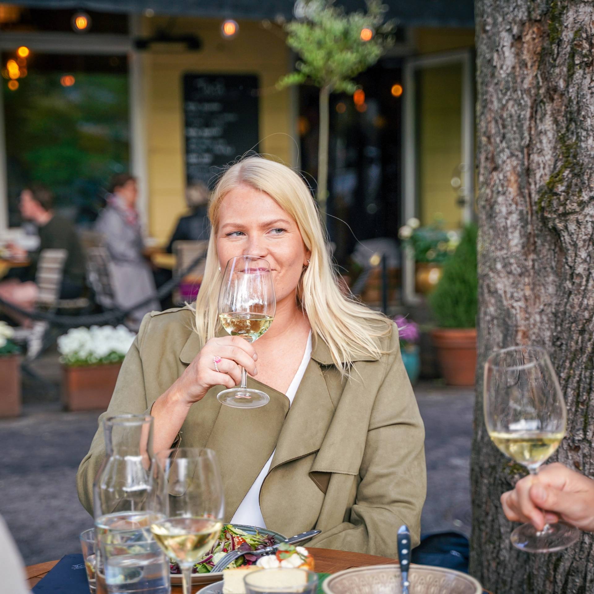 A woman drinking white wine at an outdoor restaurant table