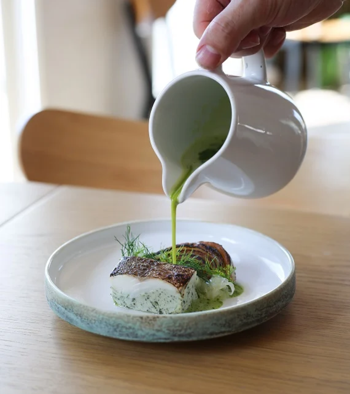 A close up of a hand pouring dressing to a dish