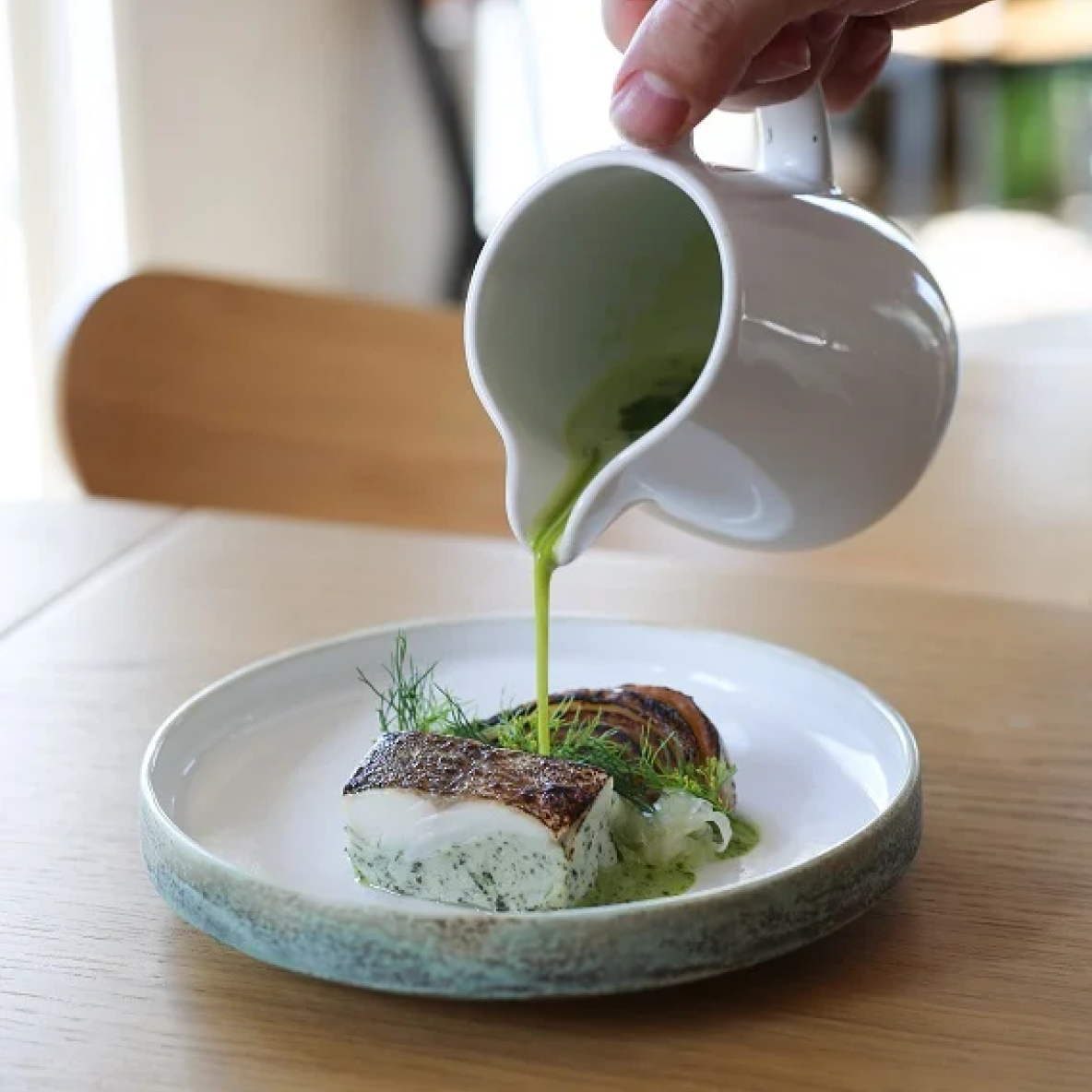 A close up of a hand pouring dressing to a dish