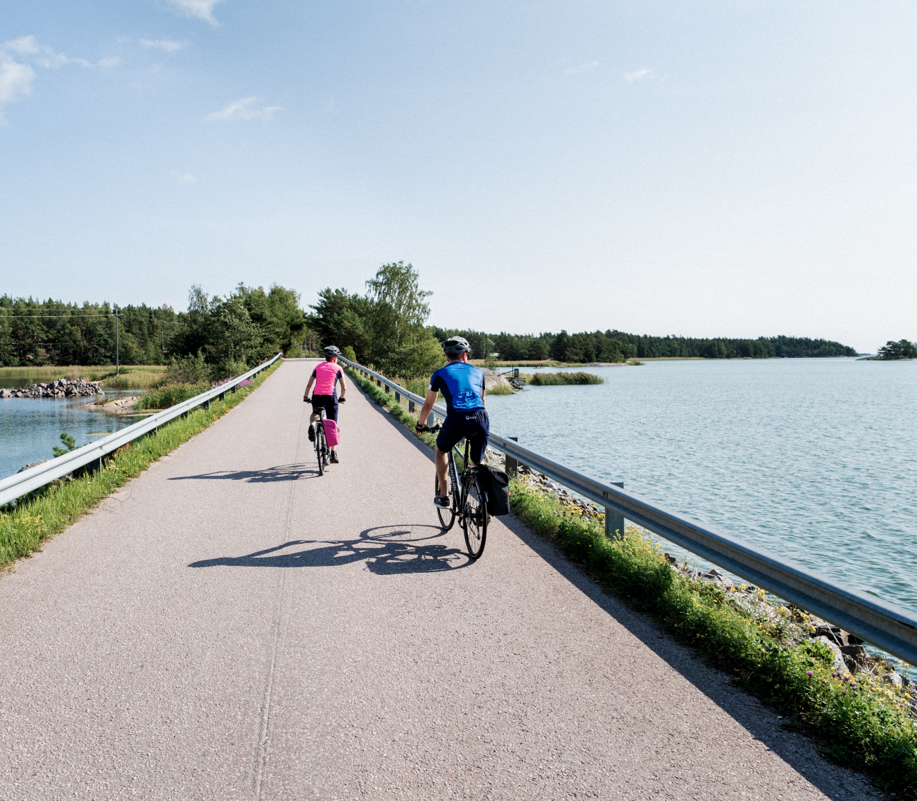 Two people crossing by bicycle a bridge overlooking a Finnish landscape.